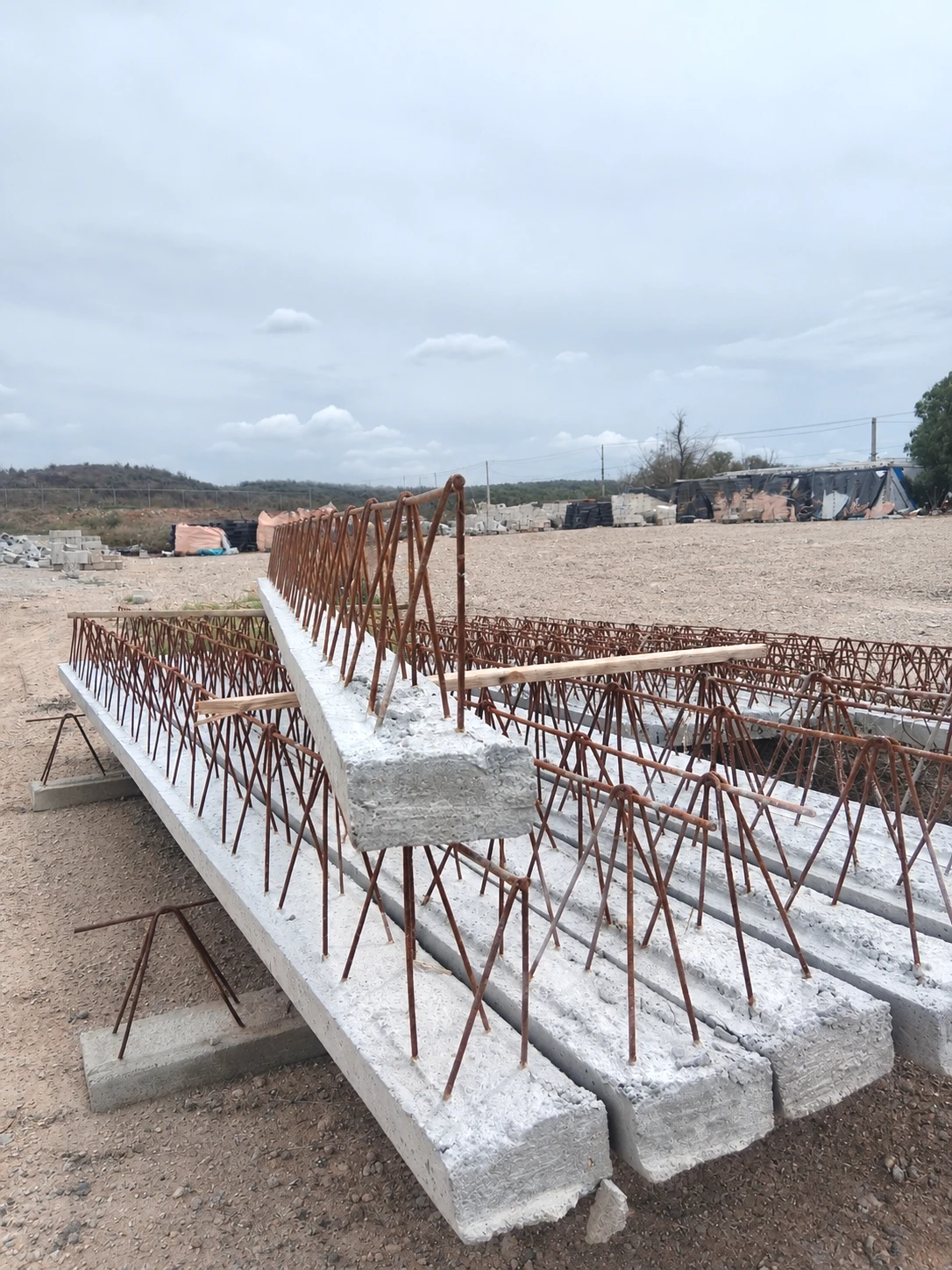 Viguetas de alma abierta 21-64 con base de concreto y armadura de acero expuesta, apiladas en el patio